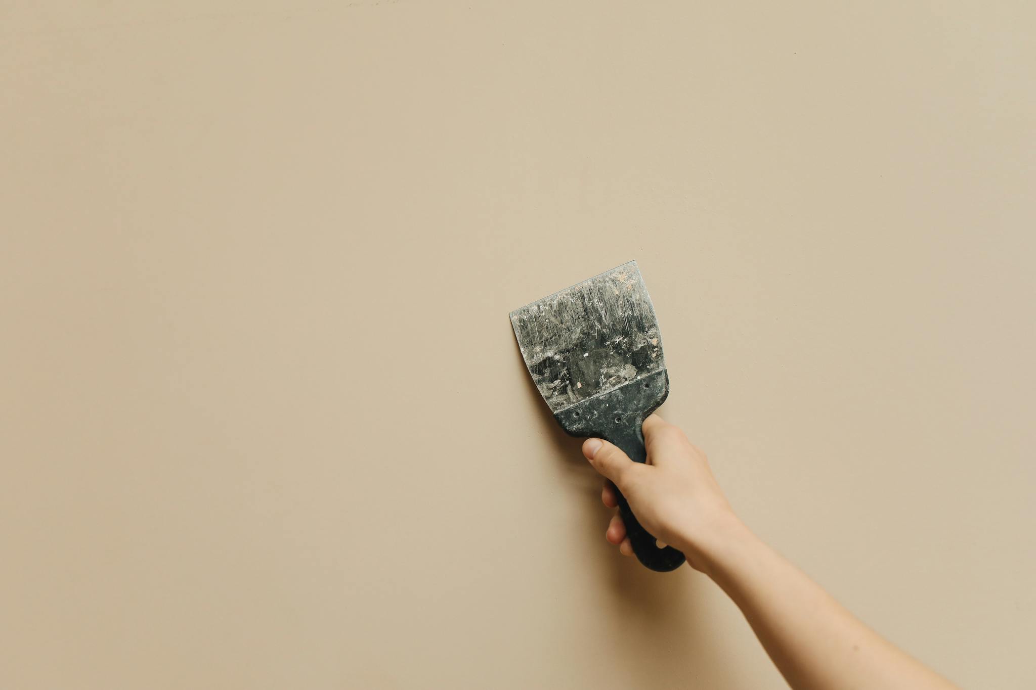 A hand holding a spatula against a blank beige wall for home renovation.